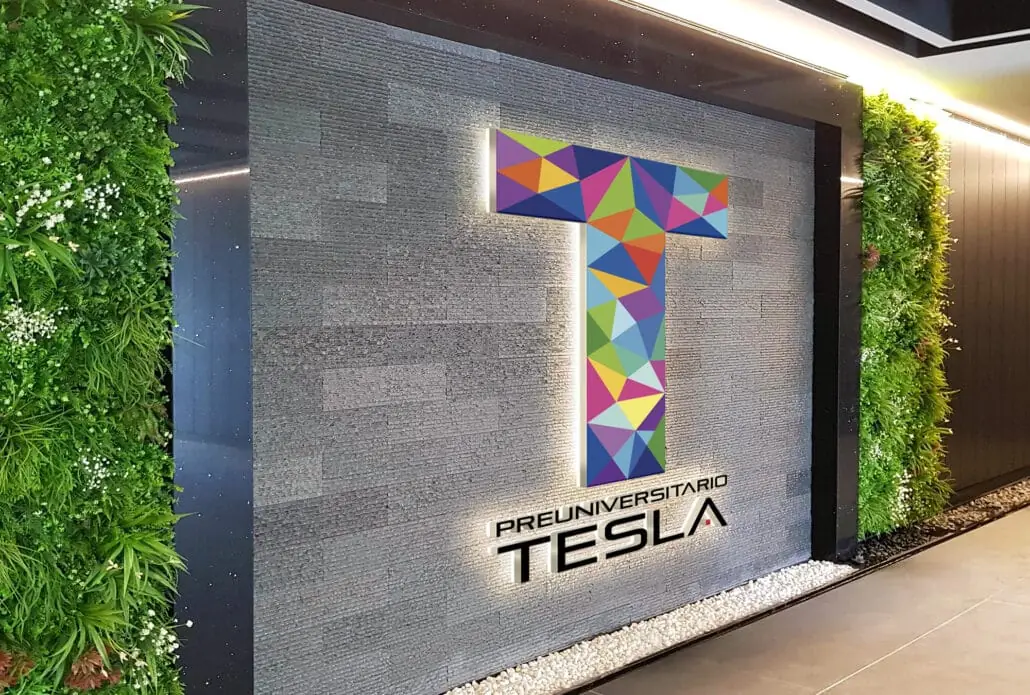 Muro de la sede del Preuniversitario Tesla con su logo iluminado entre jardines verticales